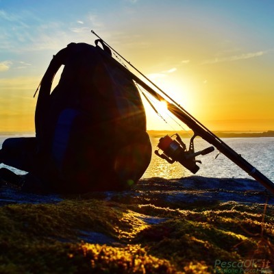 zaino e canna da pesca su scoglio al tramonto