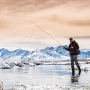 Pescatore in riva ad uno specchio d'acqua circondato da un paesaggio invernale